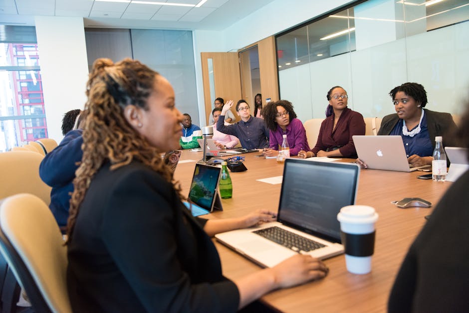 A diverse group of professionals engaging in a team meeting with laptops and discussions in a modern office setting